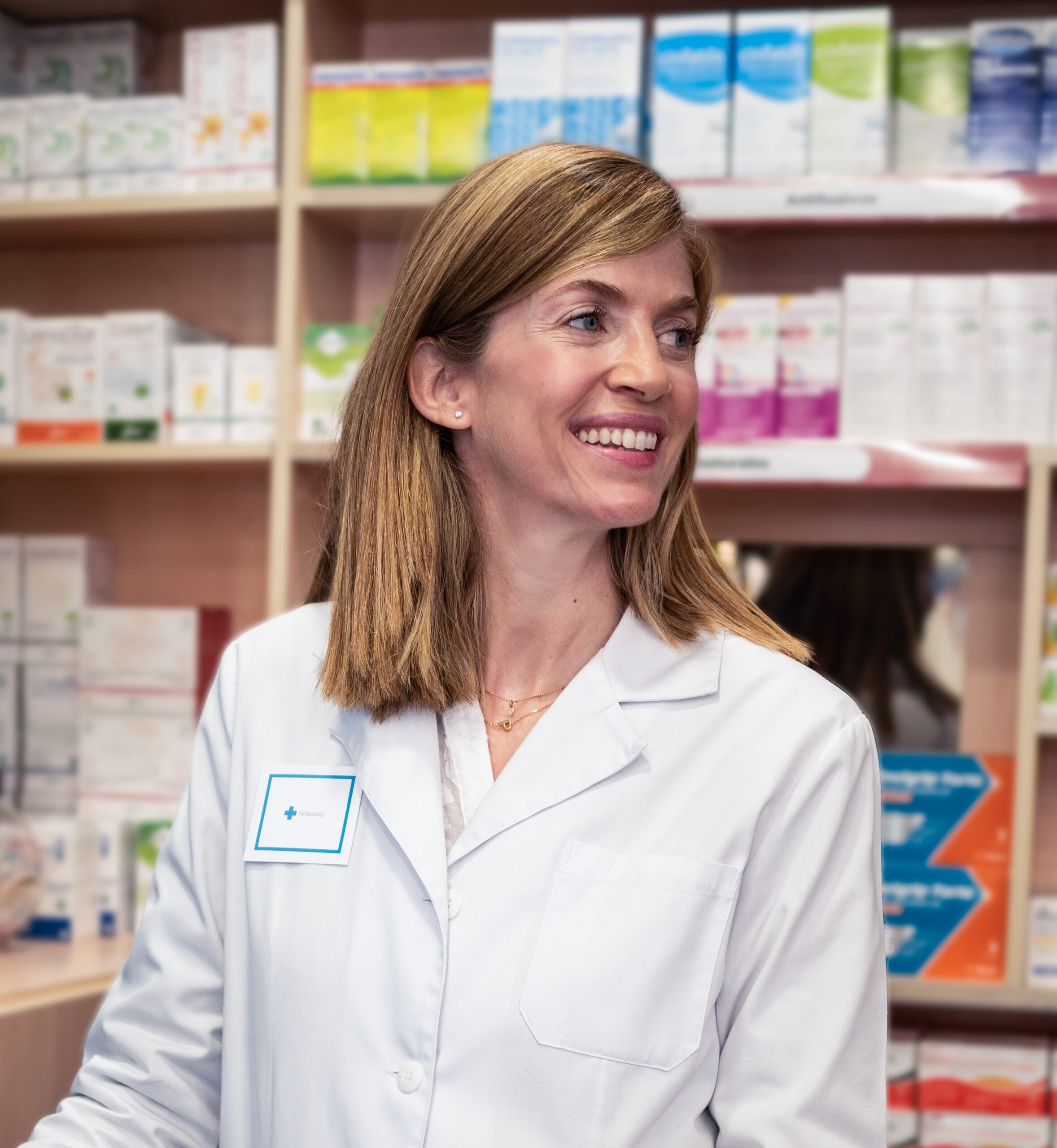 Vrouwelijke apotheker met witte schort staat achter computer in apotheek.